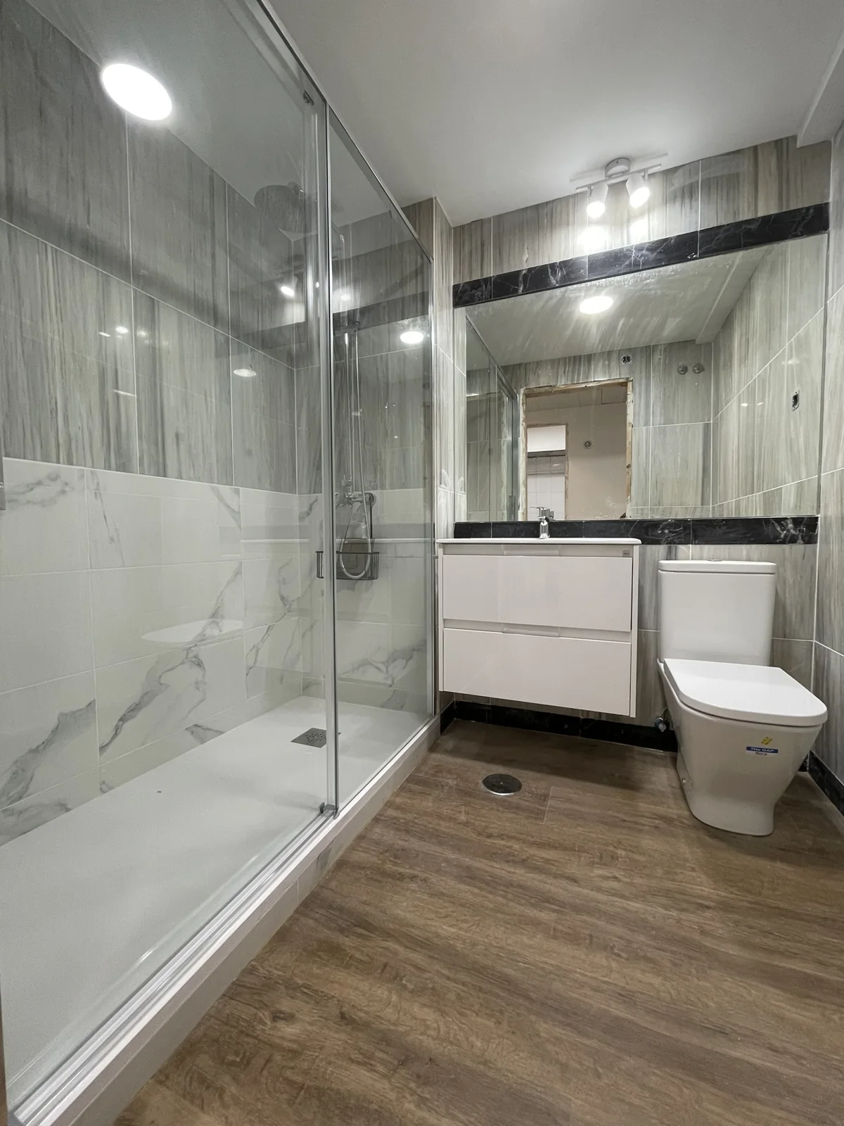 Baño terminado con ducha, mampara y suelo vinílico en un piso de Madrid centro