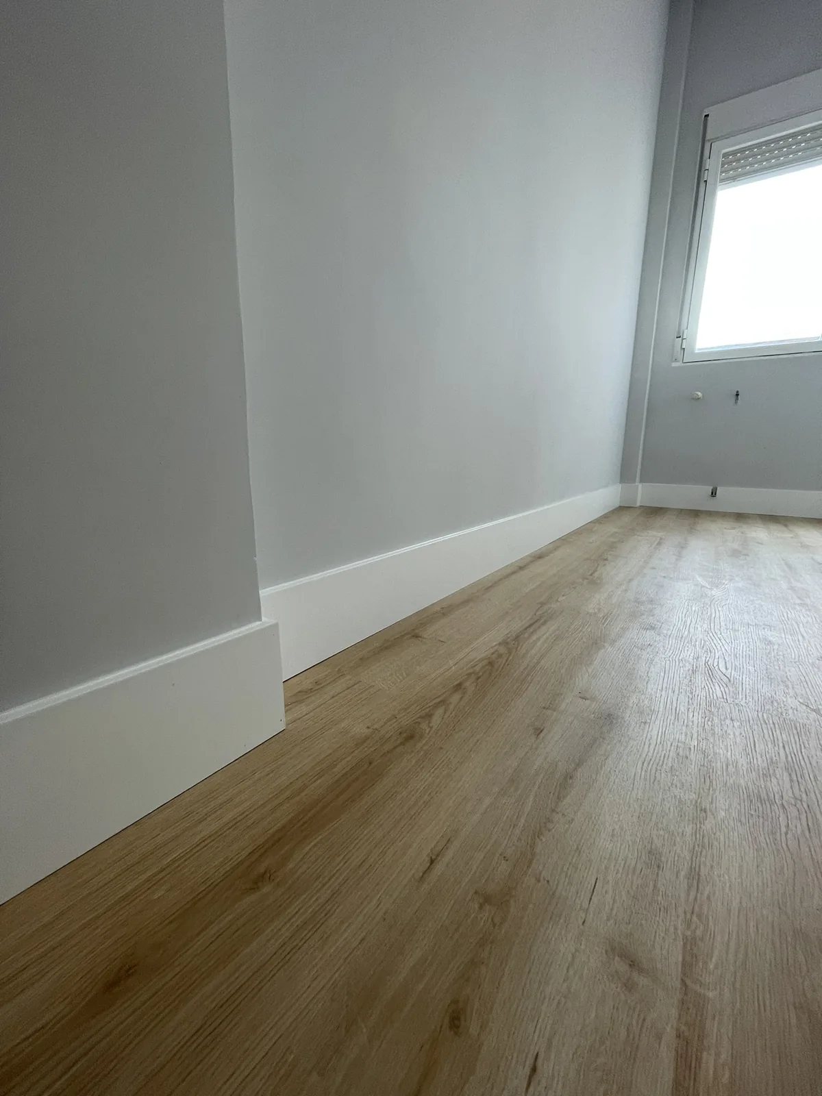 Detalle del rodapié blanco y del acabado del suelo junto a la pared.